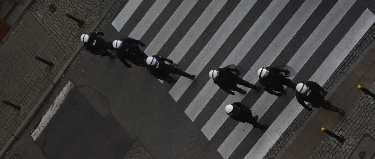 Line of helmeted police crossing a zebra crossing seen from above